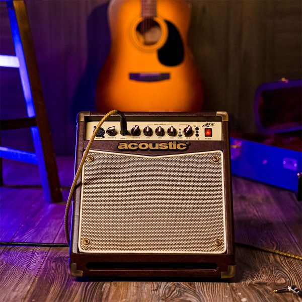 A15V 15W acoustic amp in a studio with guitar in the background and guitar case on the side